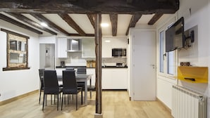 Eine moderne Küche mit weißen Schränken, ein Essbereich mit Holztisch und -stühlen sowie eine rustikale Decke mit freiliegenden Balken.