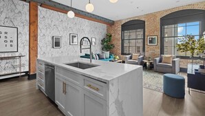 A modern kitchen with a marble island, pendant lights, and a brick wall.