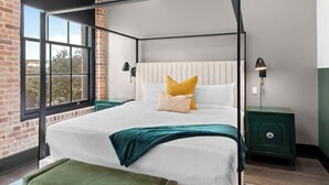 Ein Bett mit Baldachin, ein weißer Kopfteil, zwei Nachttischlampen, ein grüner Nachttisch und ein Blick durch ein großes Fenster.