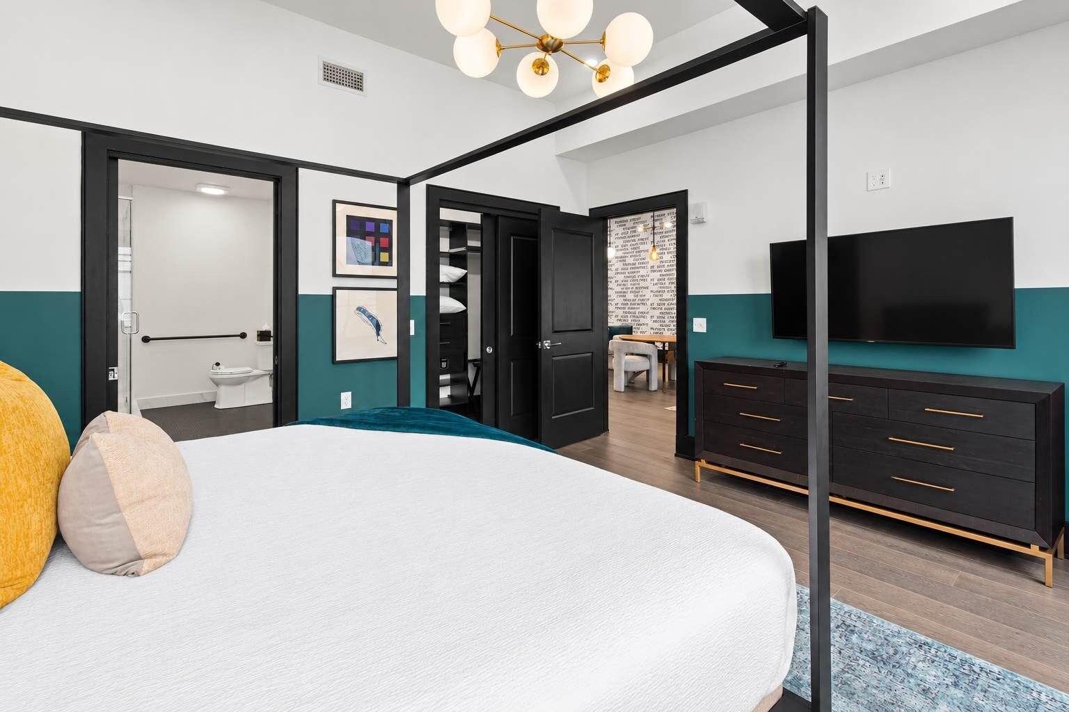 A modern bedroom with a large bed, a TV, a wardrobe, and a bathroom visible through an open door.