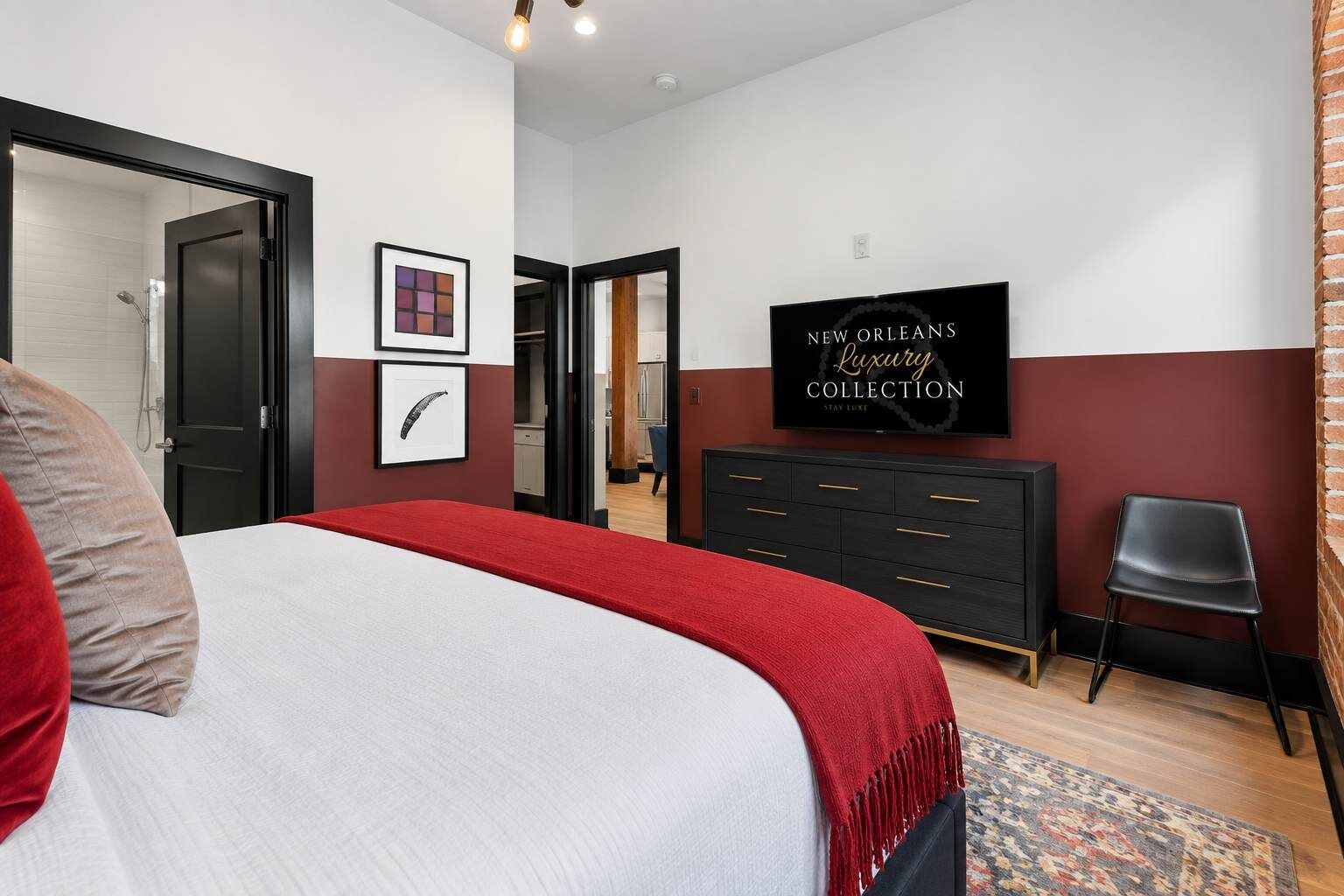 A bedroom with a bed, a dresser, a TV, and a door leading to a bathroom.