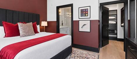 Habitación de hotel con cama, mesita de noche, escritorio, silla, armario y baño visible a través de una puerta.