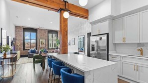 A modern kitchen with white cabinets, a marble island, and blue bar stools.