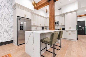 A modern kitchen with white cabinetry, a marble island, and a stainless steel refrigerator.