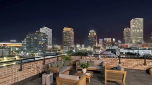 A rooftop terrace with outdoor furniture, a brick wall, and a city skyline view at night. - Downtown 4BD 4BA Suite Sleeps 12 Hotel (New Orleans)