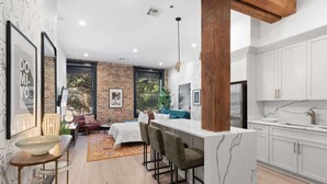 A modern kitchen with white cabinets, a marble countertop, and a large island with bar stools. - Downtown 4BD 4BA Suite Sleeps 12 Hotel (New Orleans)