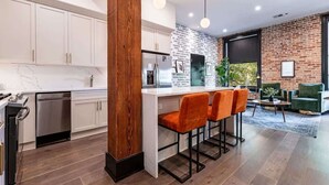 Una cocina moderna con armarios blancos, un pilar de madera y una zona de bar con sillas naranjas.