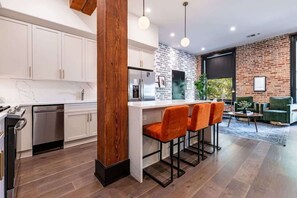 A modern kitchen with white cabinets, a wooden column, and a bar area with orange chairs. - Downtown 4BD 4BA Suite Sleeps 12 Hotel (New Orleans)