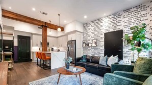 A modern living room with a sofa, coffee table, and a kitchen area with bar stools. - Downtown 4BD 4BA Suite Sleeps 12 Hotel (New Orleans)