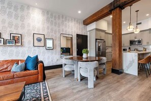 Una cucina moderna con mobili bianchi, un'isola centrale e un'area pranzo con tavolo in legno e sedie rivestite di grigio.