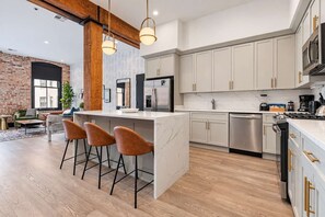 Una cocina moderna con una isla central, taburetes de bar, electrodomésticos de acero inoxidable y armarios de color claro.