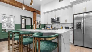 A modern kitchen with white cabinets, a stainless steel refrigerator, and a bar area with green upholstered chairs. - Suite Double The Space XL Hotel 2 Living Rooms Kitchens (New Orleans)