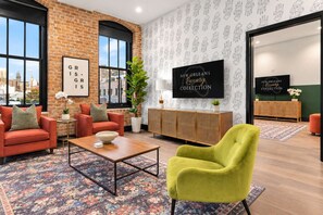 A modern living room with a brick wall, large windows, a sofa set, a coffee table, and a television displaying a collection.