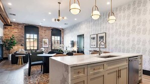 A modern kitchen with a central island, pendant lighting, and a brick wall.
