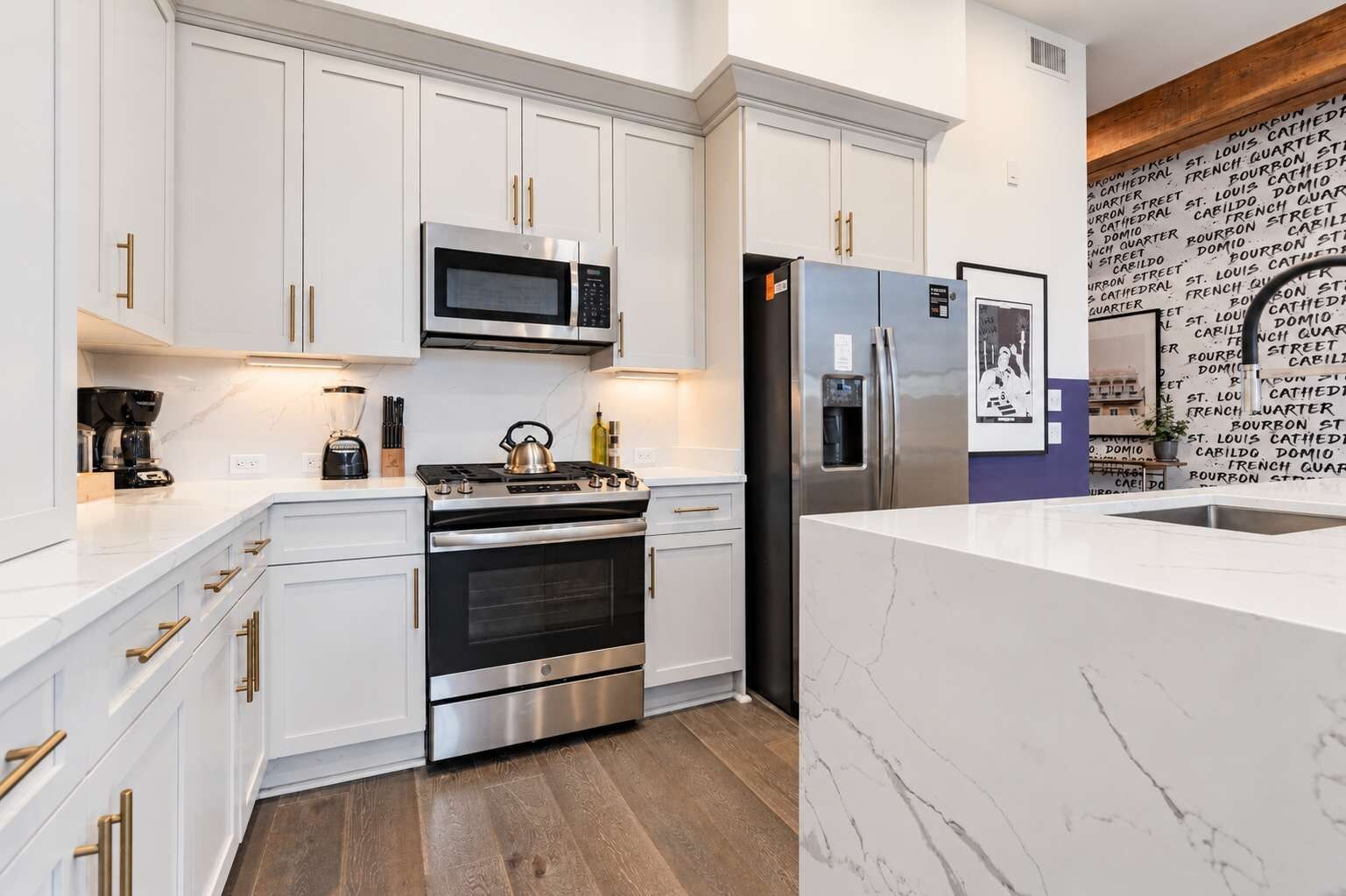 A modern kitchen with white cabinetry, stainless steel appliances, and a marble countertop.