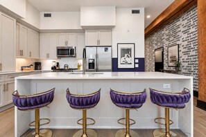 A modern kitchen with white cabinetry, stainless steel appliances, and a central island with bar stools.