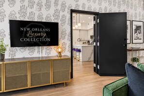 Un interno moderno con un mobile nero, una televisione che mostra 'NEW ORLEANS Luxury Collection' e un'apertura che dà su un angolo cottura.