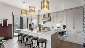 A modern kitchen with a central island, bar stools, pendant lights, and white cabinetry. - Downtown Corner Penthouse w Private Terrace Suite Hotel (New Orleans)
