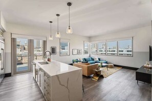 A modern apartment with a kitchen, living area, and large windows offering city views. - Corner Penthouse w/ Private Balcony- Hotel (New Orleans)