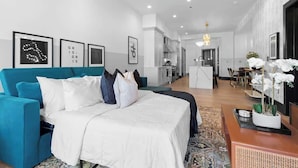 A modern hotel room with a bed, a sofa, a dining area, and a kitchen in the background. - LUX Suite Rooftop Pool Workspace Games Hotel (New Orleans)