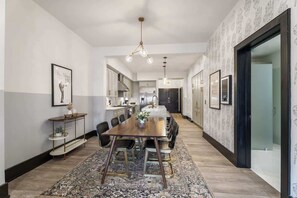 Un espace repas comprenant une longue table en bois, des chaises, un tapis à motifs et un lustre.