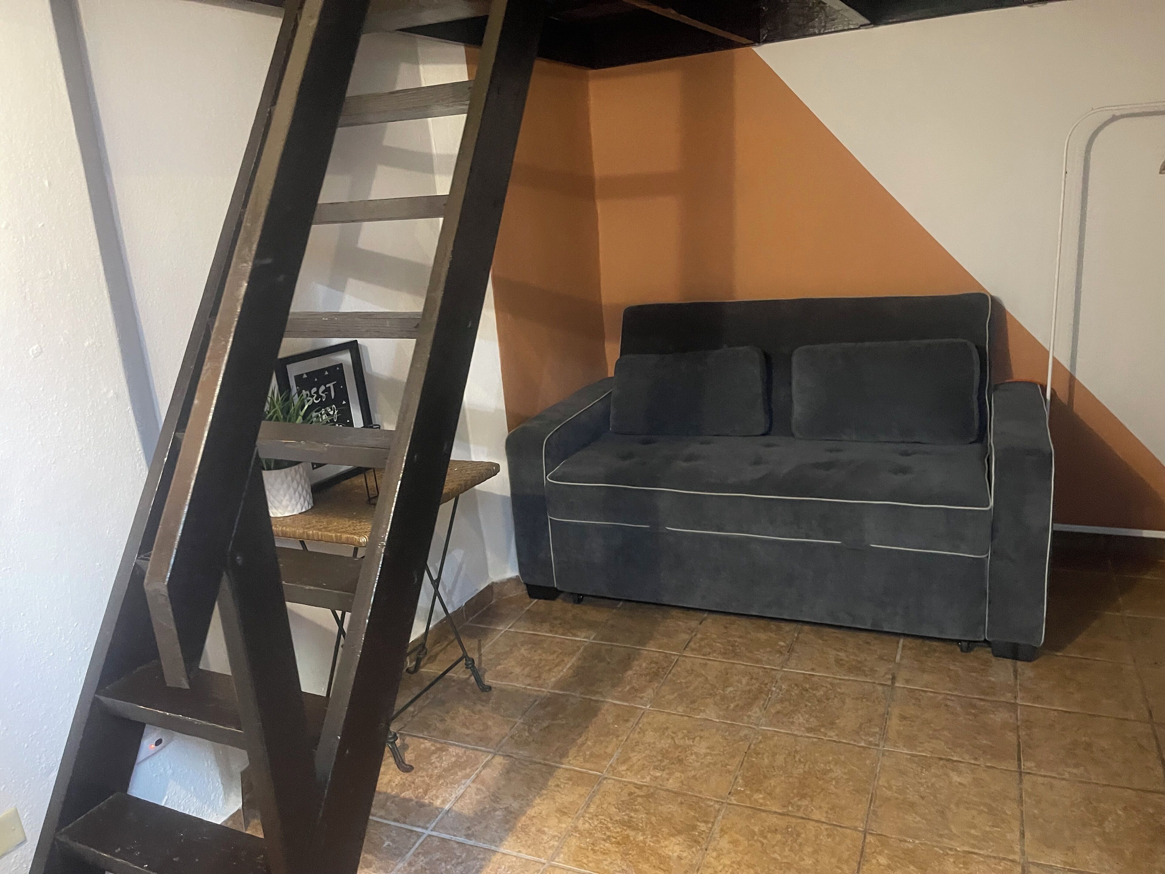 A room with a black sofa, a wooden ladder, and a tiled floor.
