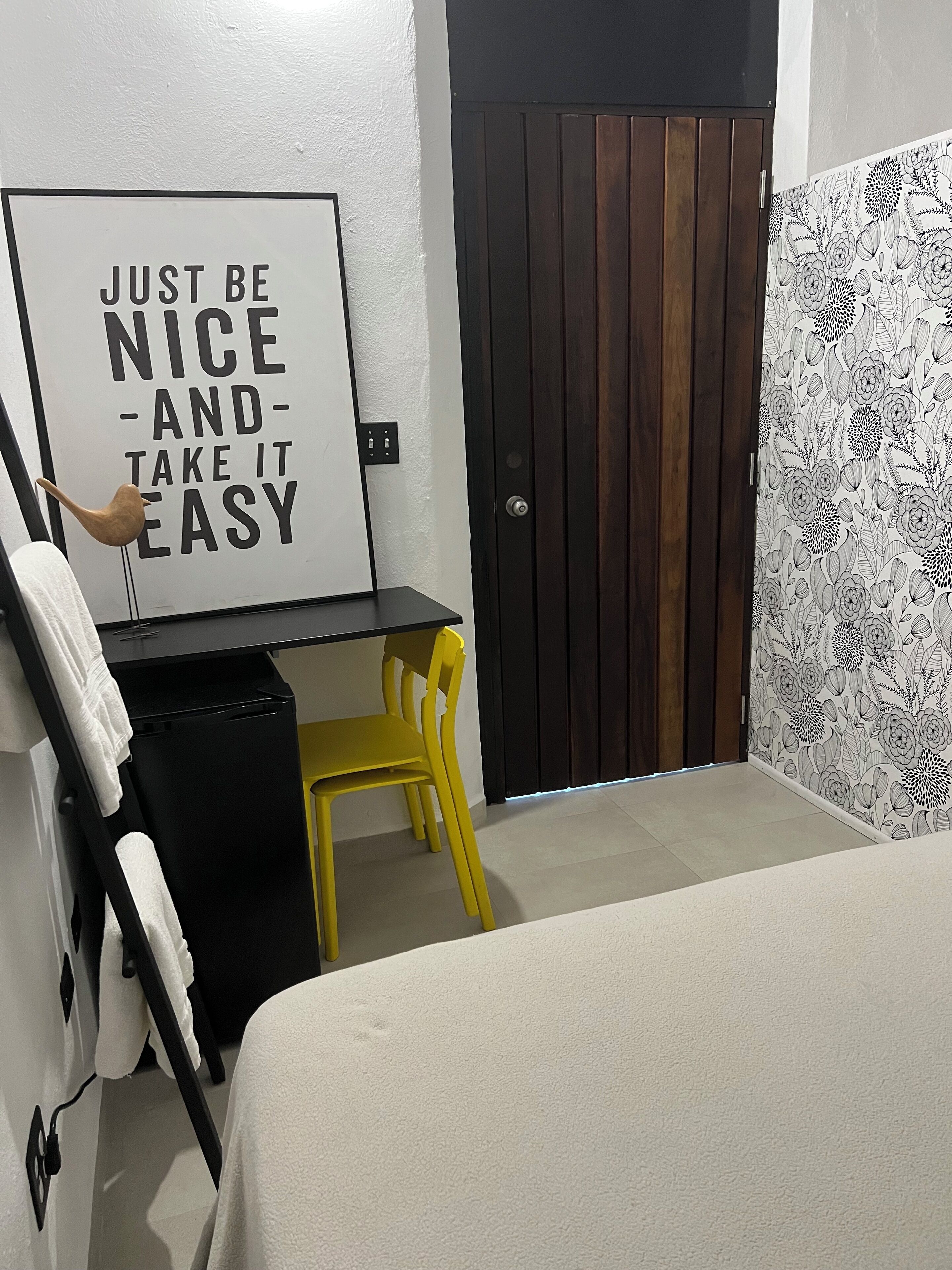 Slaapkamer met een bed, een bureau, een stoel, een muur met een motiverende quote, een deur en een behang met een patroon.