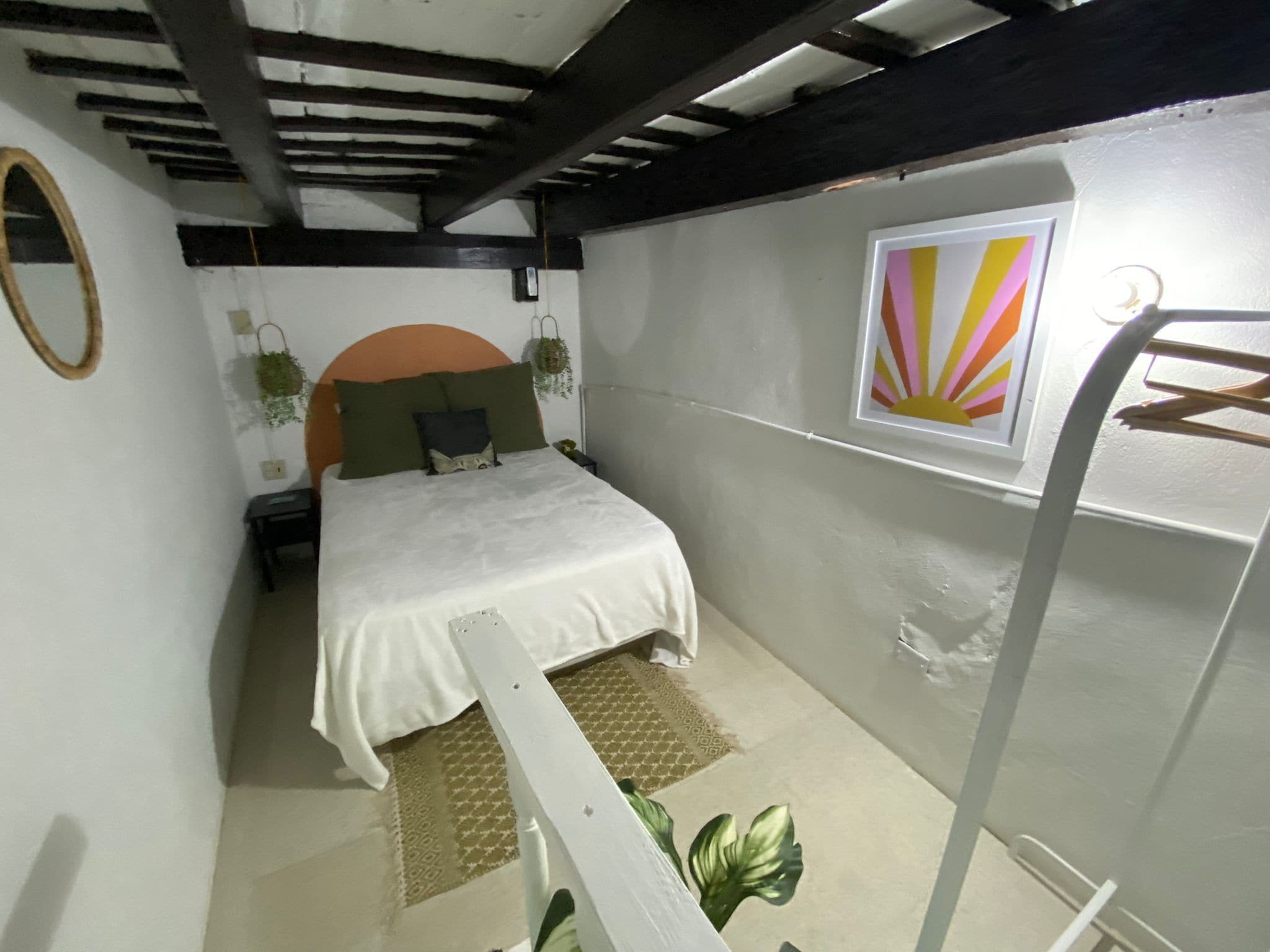 Ein Schlafzimmer mit einem Bett, einem Nachttisch, einem an der Wand befestigten Regal, einer hängenden Pflanze und einem Fenster mit Sonnendesign.