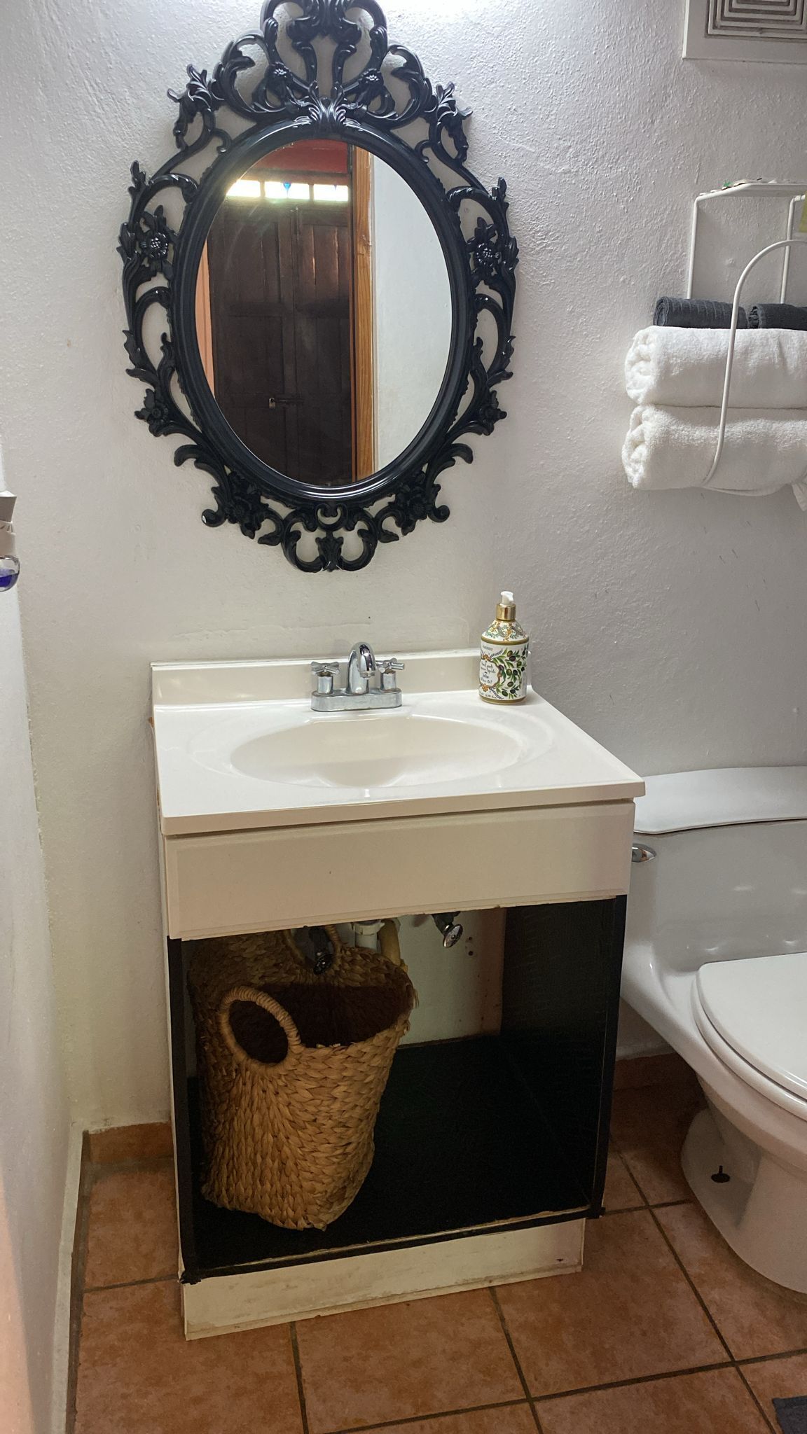 A bathroom with a white sink, a mirror with an ornate black frame, a toilet, and a towel rack with towels.