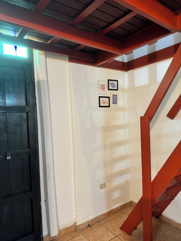 A staircase with red railings leading to an upper floor, a white door with a padlock, and a wall with framed pictures.