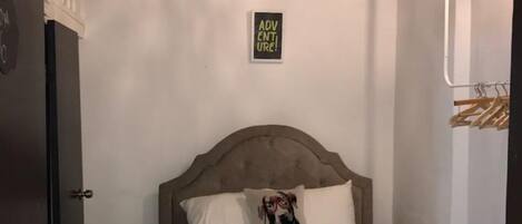 Quarto com cama, luminária pendente, mesinha de cabeceira e placa na parede.