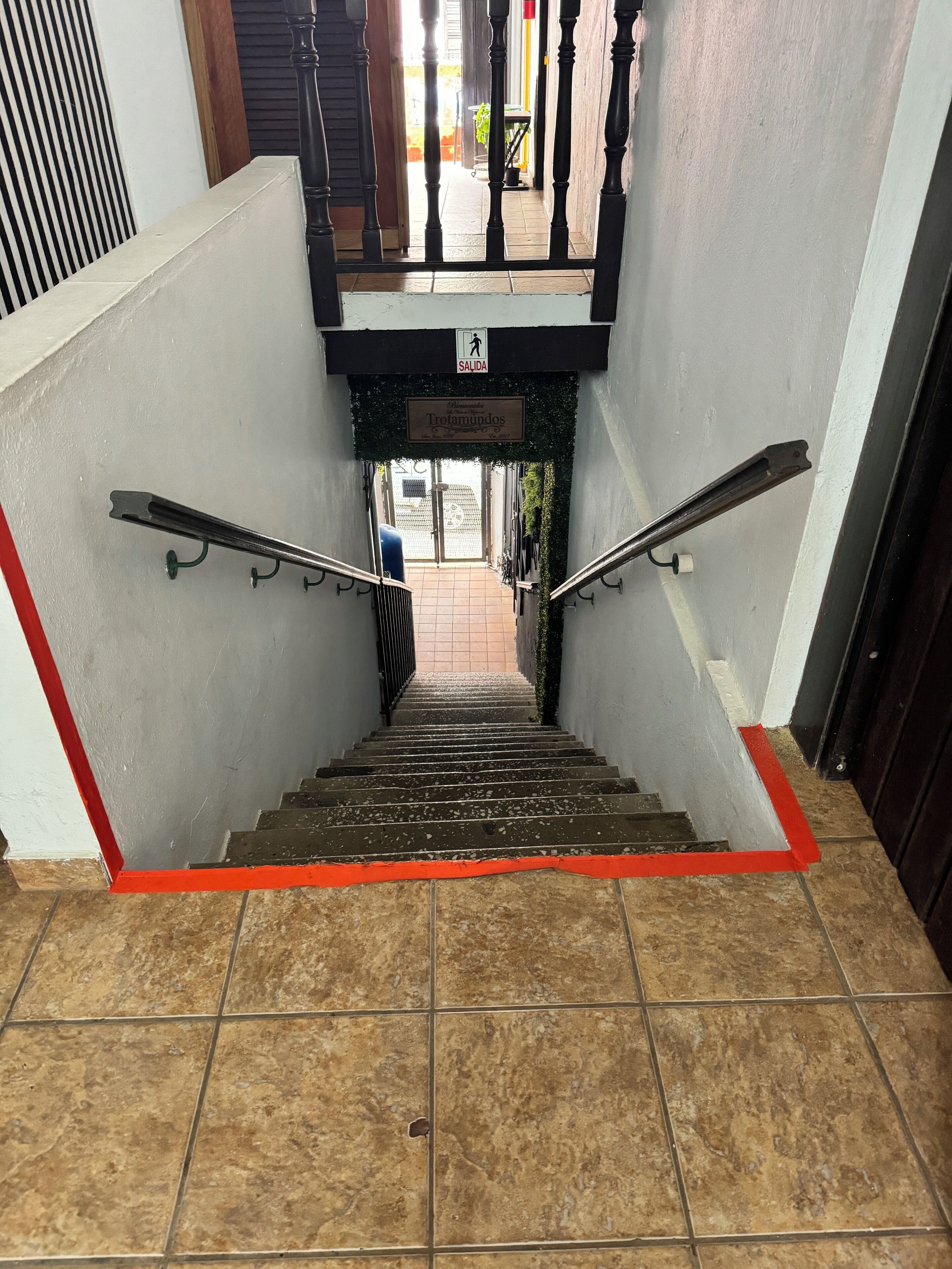 A staircase with a red safety strip, metal handrails, and a sign indicating an exit.