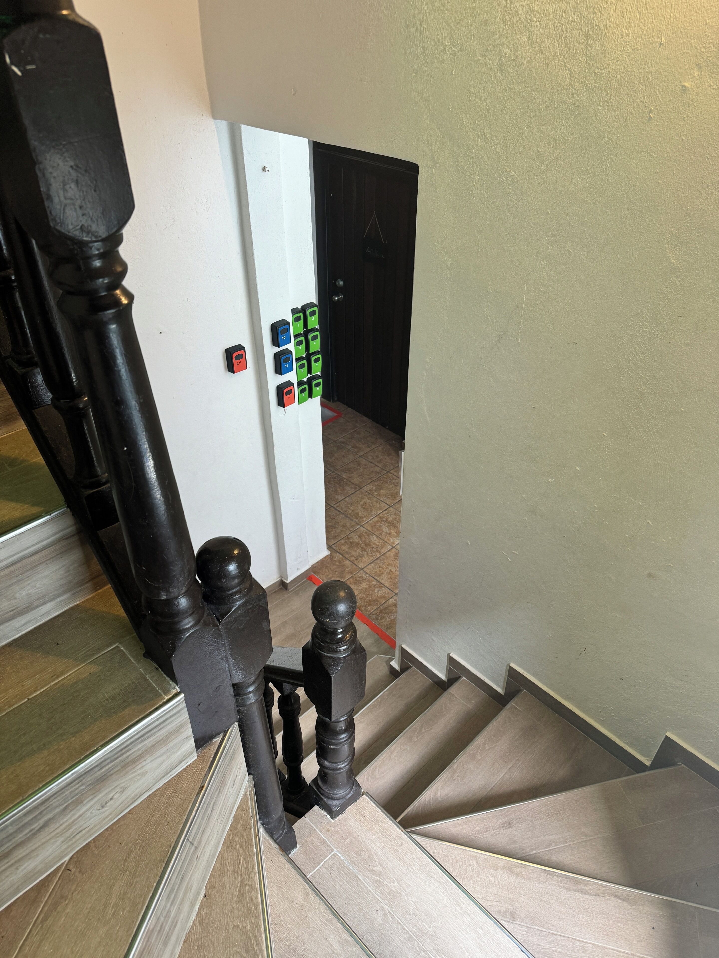 Un escalier avec une rampe, une porte dotée d’un clavier pour l’ouverture, et un sol carrelé.