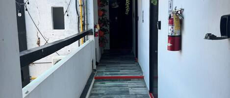 A narrow corridor with a blue canopy, potted plants, a fire extinguisher, and a red fire hose.