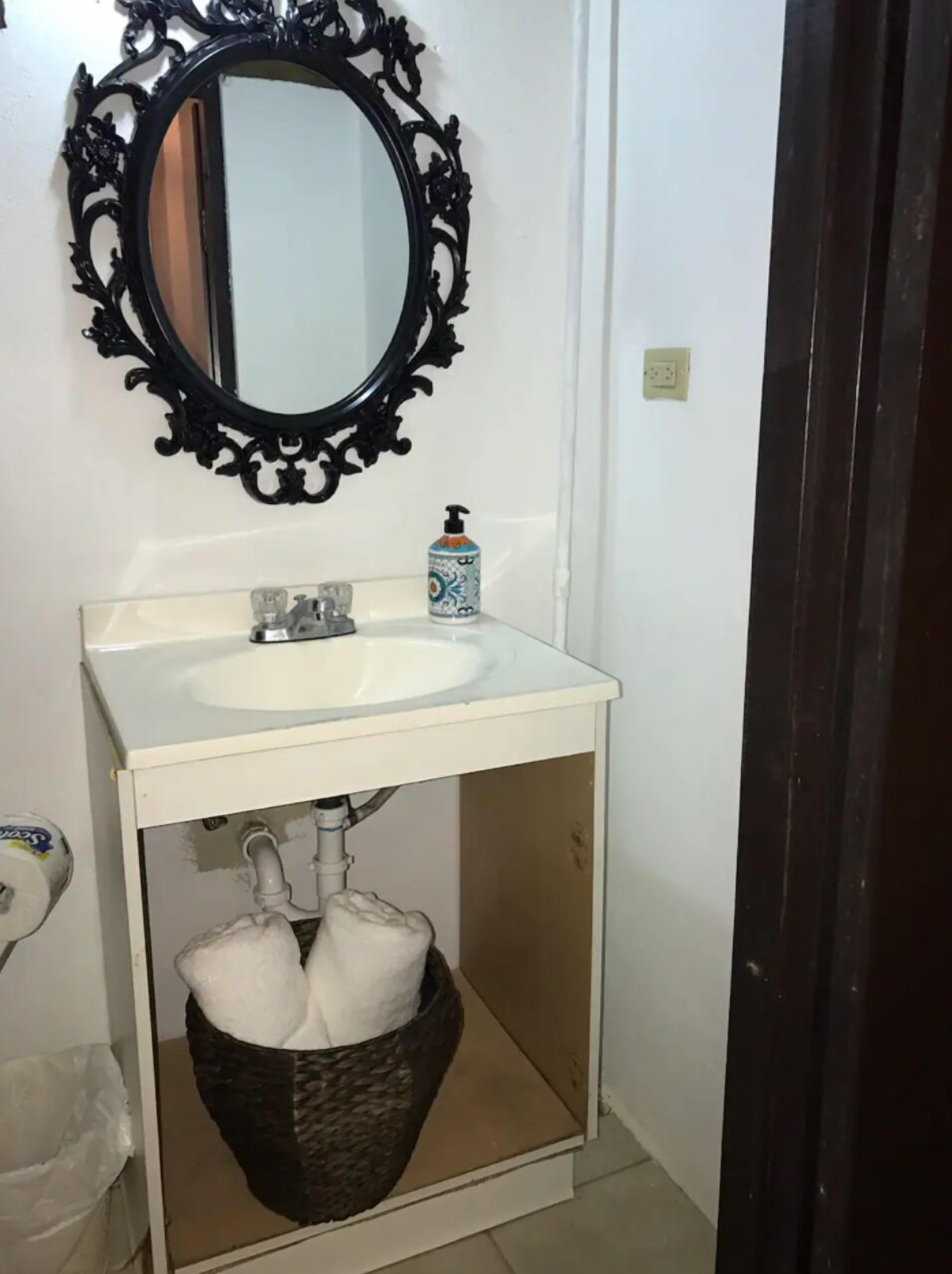 Un baño con un lavamanos blanco, un espejo negro ornamentado y un dispensador de jabón.
