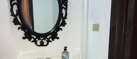 Un baño con un lavamanos blanco, un espejo negro ornamentado y un dispensador de jabón.