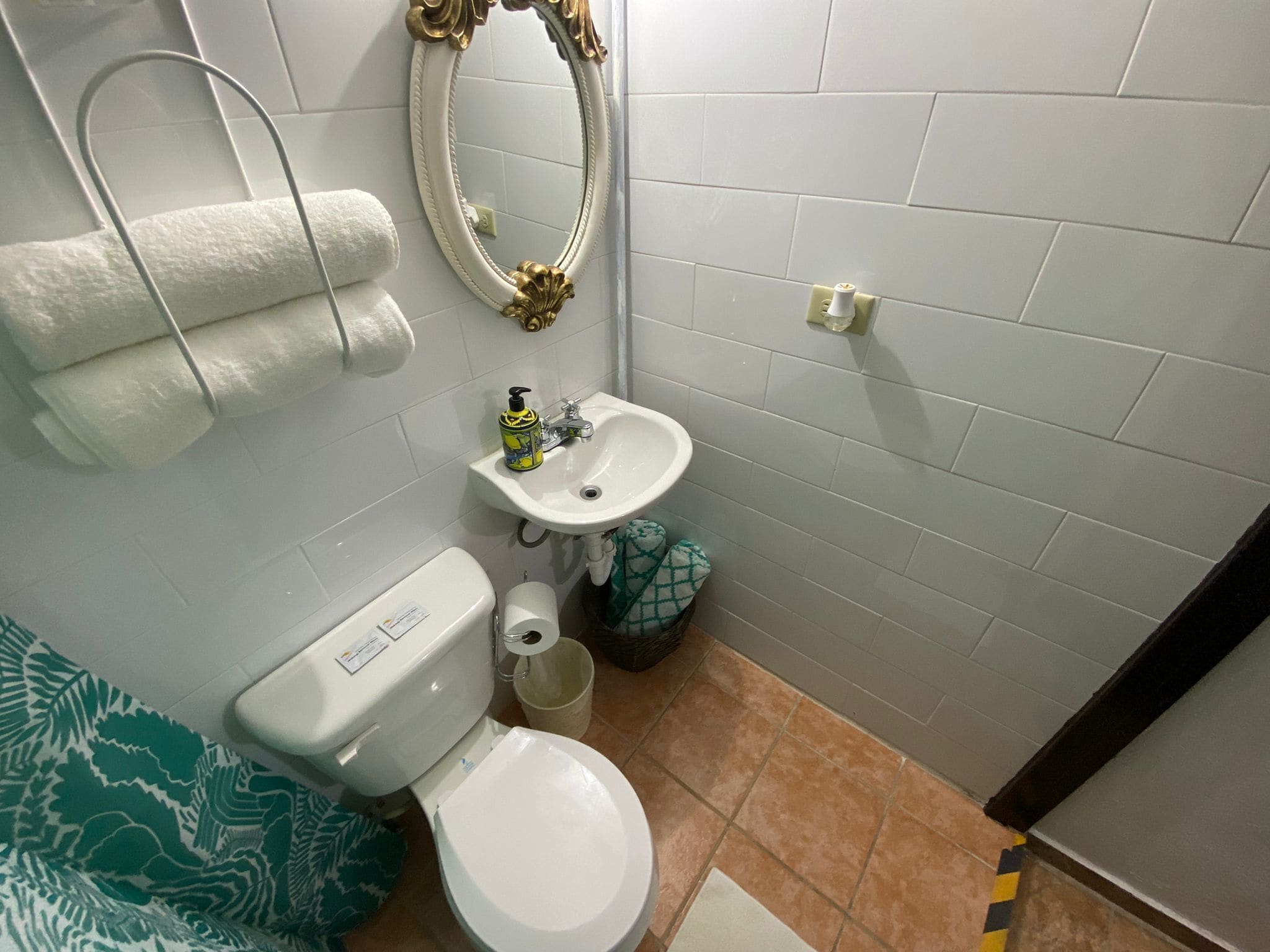 A bathroom with a toilet, sink, and mirror. There are towels and a trash bin.