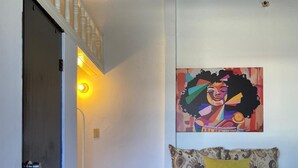 Een slaapkamer met een bed, een schilderij aan de muur, een klein krukje en een deur.