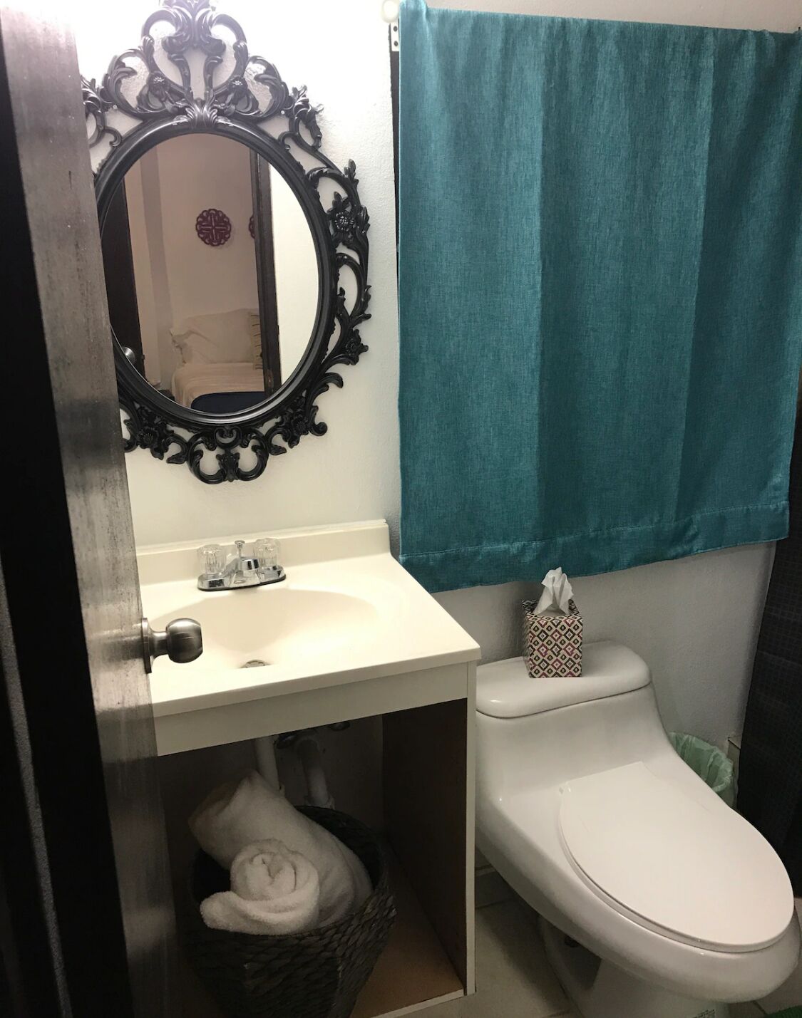 Une salle de bain avec un lavabo blanc, un miroir doté d’un cadre orné, des toilettes et une serviette turquoise accrochée au mur.