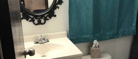 Une salle de bain avec un lavabo blanc, un miroir doté d’un cadre orné, des toilettes et une serviette turquoise accrochée au mur.