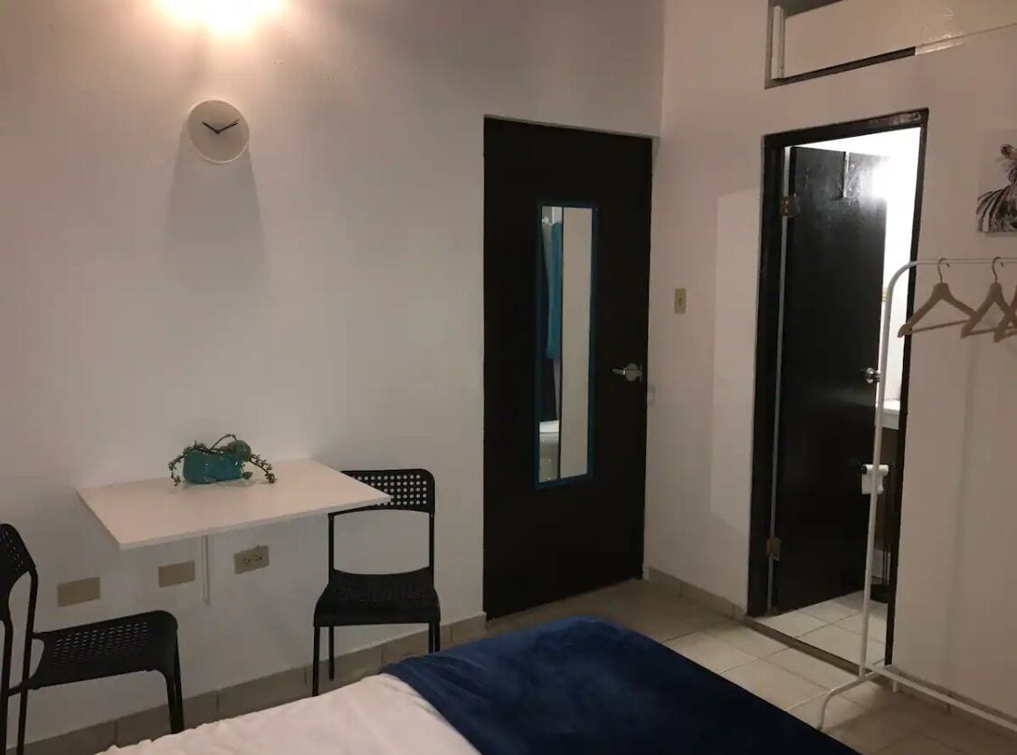 A bedroom with a bed, a desk with a chair, a wardrobe, and a mirror.
