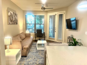A living room with a sofa, coffee table, TV, and a ceiling fan. - MCK104 - Apt|Patio|15mi to Toyota Stadium|Sleeps 2 (McKinney)