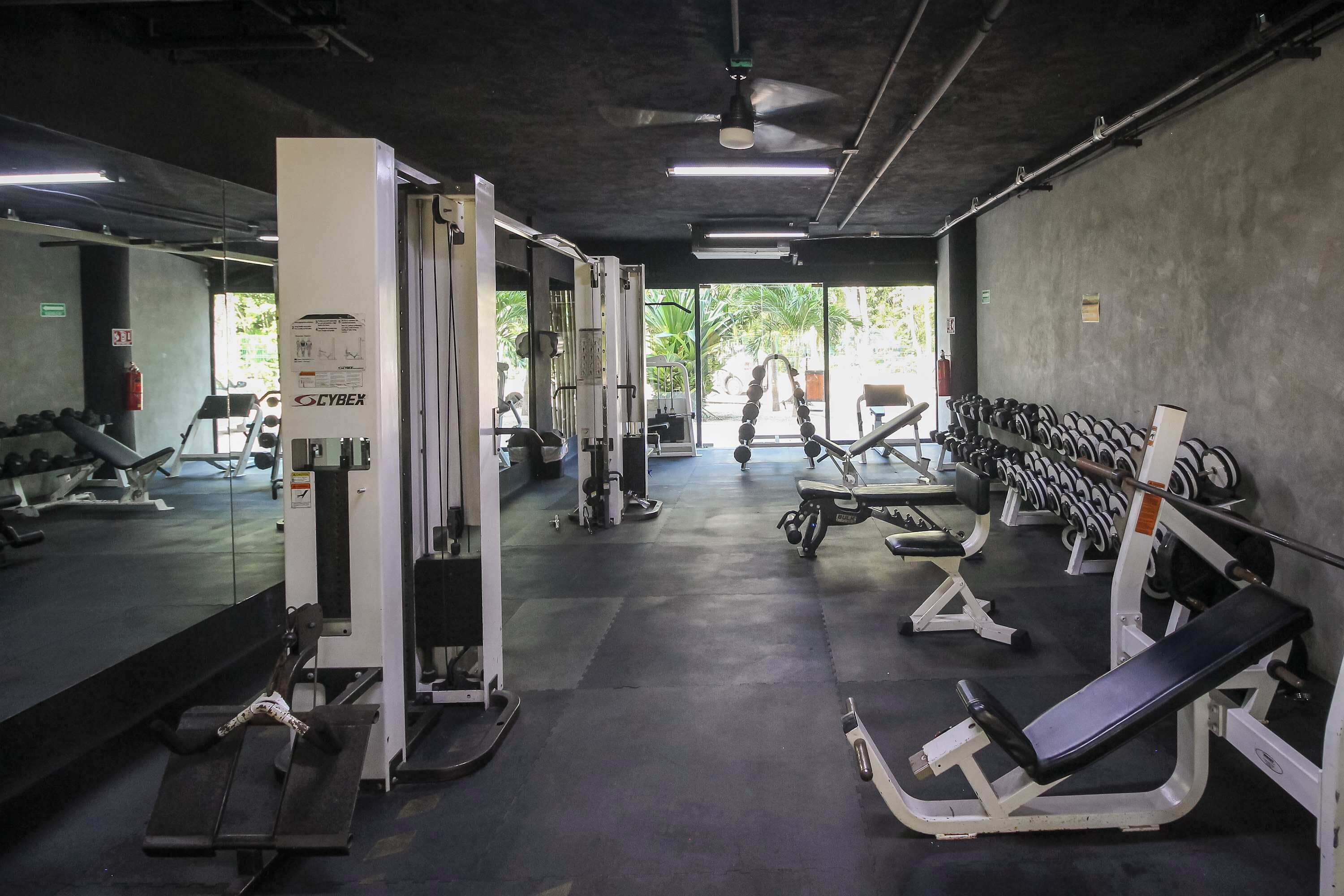 A gym with exercise equipment, mirrors, and a ceiling fan.