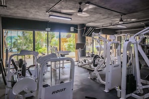 Ein Fitnessstudio mit verschiedenen Trainingsgeräten, großen Fenstern und einem Deckenventilator.