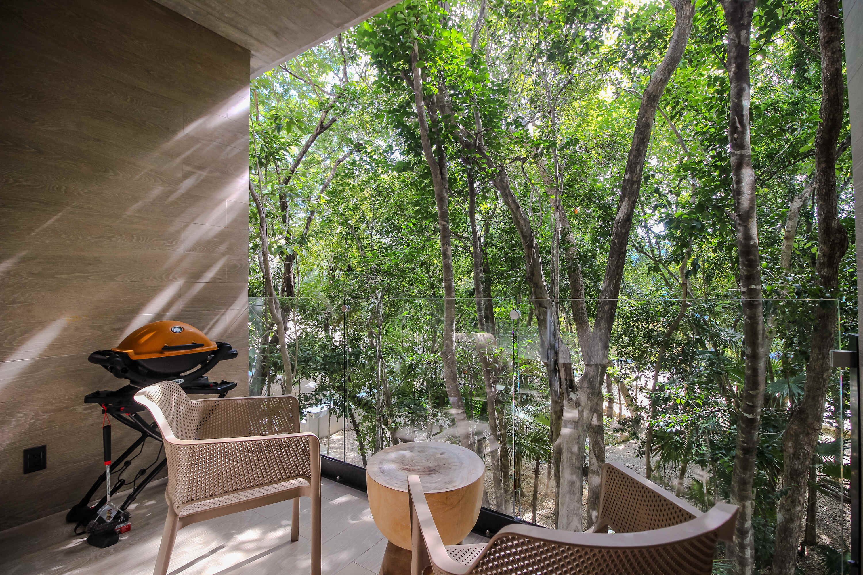 A room with a view of a forest, a wooden table, and two wicker chairs.