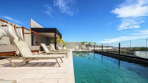 A rooftop pool with clear water, lounge chairs, and a modern building structure.