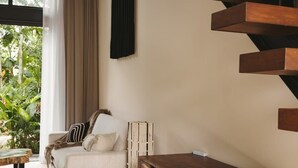 A modern room with a wooden staircase, a sofa with cushions, a dining table, and a wicker chair. - Luxury Loft w/ Pool, Gym & Rooftop Panoramic Views (Tulum)