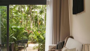 A modern living room with a large glass door leading to a lush garden. - Luxury Loft w/ Pool, Gym & Rooftop Panoramic Views (Tulum)