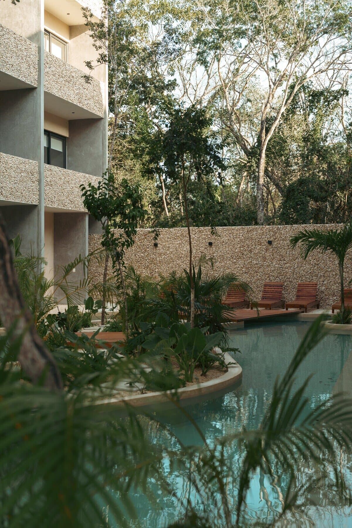 A pool area with lounge chairs and a stone wall.