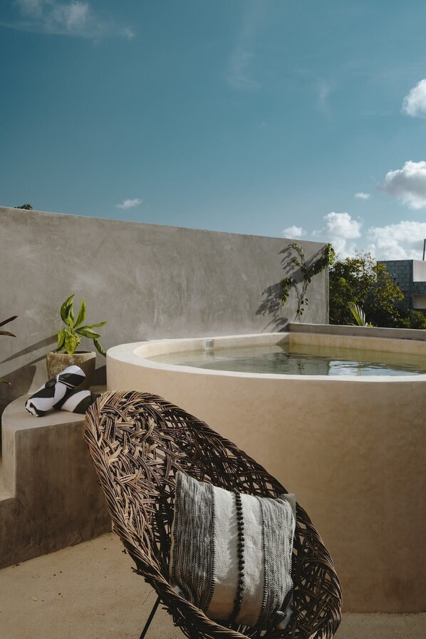A hot tub with a concrete wall, a wicker chair with a striped cushion, and a small potted plant. - Casa Felipa | Chic Jungle Hideaway w/ Private Pool (Tulum)
